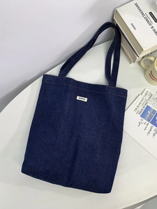 Close-up of dark blue denim tote bag with ATRYG label on a white table with books