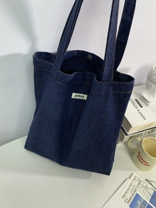 Detailed view of dark blue denim tote bag with ATRYG woven label in a lifestyle setting