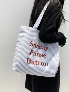 Gros plan d'un cabas en toile rayée avec texte rouge Sunday Pause Button porté par un mannequin