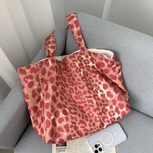 Detailed close-up of pink leopard print canvas tote bag on grey sofa with casual props