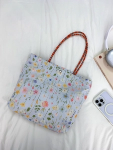 Detail of floral embroidery on light blue canvas bag with woven handle and magnetic closure