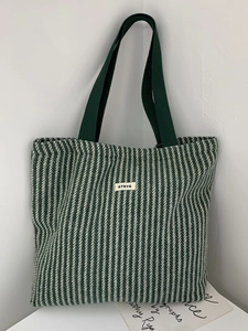 Detailed view of green herringbone wool tote bag featuring a square logo patch and handles