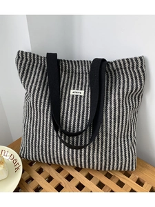 Detail of herringbone woven fabric tote bag with black strap handles and logo patch