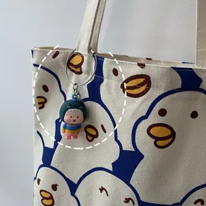 Close-up of cute cartoon dinosaur plush keychain accessory on a white canvas tote bag