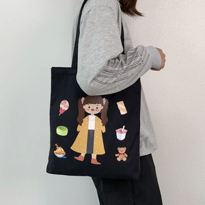 Detail shot of a black canvas tote bag featuring cute cartoon girl and candy prints