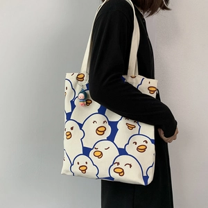 Detail of off-white canvas tote bag featuring cute blue cartoon duck patterns and charm