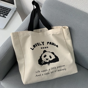 Minimalist beige canvas tote bag with cute panda print and black straps on a sofa