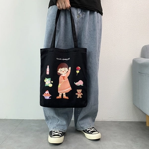 Detail of a black canvas tote bag featuring cute cartoon girl prints and a slogan