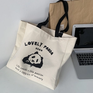 Detail shot of a cream canvas tote bag featuring a cute panda print and black straps