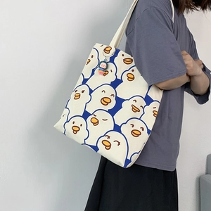 Detailed view of canvas tote bag with blue cartoon duck patterns and colorful doll pendant