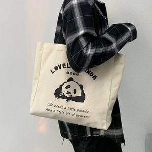 Detail of cream canvas tote bag with panda print on shoulder strap of a plaid shirt