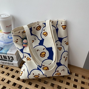 Artistic canvas tote bag with cute duck print shown on a wooden bench with lifestyle props