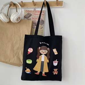 Detail view of a black canvas tote bag with cute cartoon girl and dessert illustration
