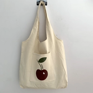 Detail of cream canvas tote bag featuring front pocket with cherry print and text