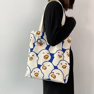 Detail of canvas tote bag featuring blue cartoon duck print and colorful doll charm