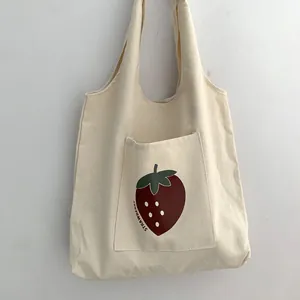 Close-up of a large front pocket with a red strawberry print on a canvas tote bag