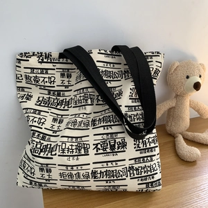 Close-up of white canvas tote bag featuring black text prints and wide shoulder straps