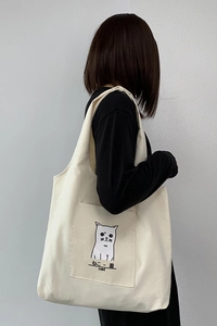 Detail view of off-white canvas tote bag featuring a minimalist cat print and front pocket
