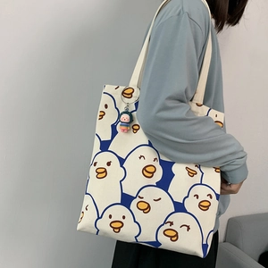 Detail of white canvas tote bag featuring cute cartoon duck patterns and a plush charm