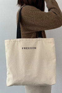 Close-up of minimalist canvas tote bag with black FREEDOM lettering and shoulder strap