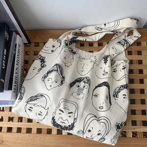 Artistic canvas tote bag with hand-drawn face patterns displayed next to art books
