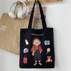 Detail of a black canvas tote bag featuring an artistic cartoon girl print on a wooden hook