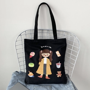 Detail of black canvas tote bag featuring a cute girl cartoon print on a mesh chair
