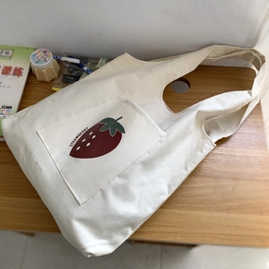 Detail of strawberry graphic and outer pocket on minimalist cream canvas tote bag
