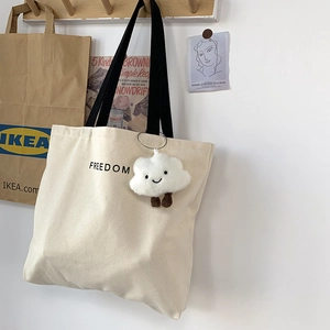 Detail of beige canvas tote with black FREEDOM letters and a cute cloud plush charm