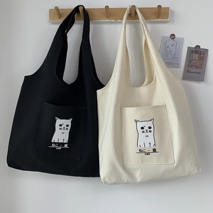 Detail of canvas tote bags in black and beige featuring cute cat pocket illustrations