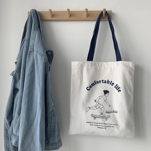 Detail of white canvas tote bag featuring skateboarder print and durable blue handles