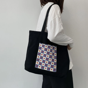 Detail of black canvas tote bag with heart checkerboard pocket shown on model shoulder