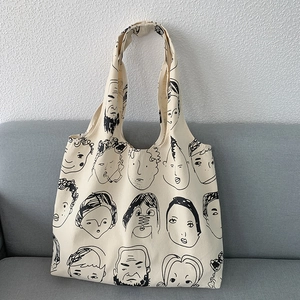 Detail shot of canvas tote bag with black portrait line art on a grey fabric sofa