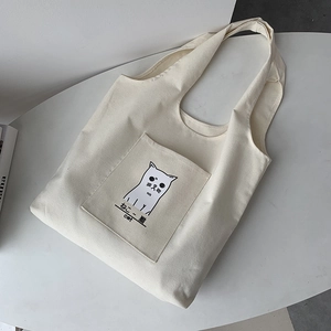 Detail of canvas tote bag with outer pocket and minimalist cartoon cat illustration