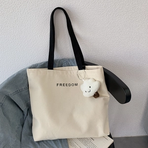 Detail view of the beige canvas tote bag with black freedom lettering and cloud charm