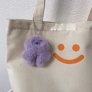 Detail of purple plush monster charm with embroidery on a white canvas tote bag
