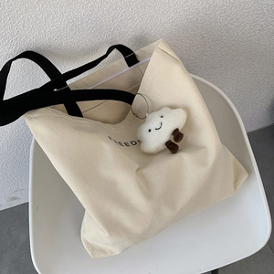 Detail of canvas tote bag with black straps, FREED lettering and a cloud charm