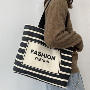 Detail of striped canvas tote bag showing Fashion Trends logo and black shoulder straps