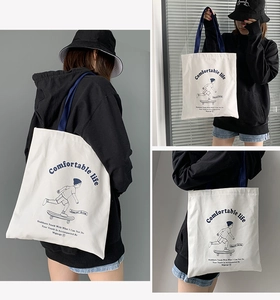 Detail of white canvas tote bag with navy blue handles and artistic letter printing