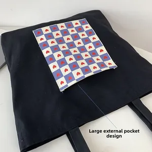 Detail view of the large outer pocket with red heart checkerboard pattern on black tote bag