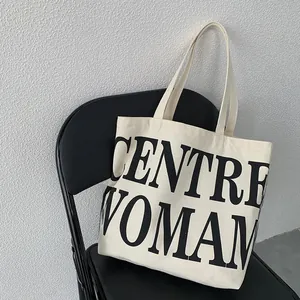 Detail of off-white canvas tote bag with black CENTRE WOMAN lettering on a chair