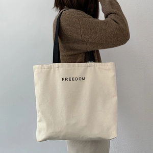 Detail of FREEDOM print on cream canvas tote bag worn by a model on her shoulder