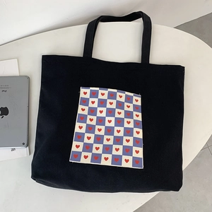 Detail of black canvas tote bag featuring a blue checkered heart pocket for students