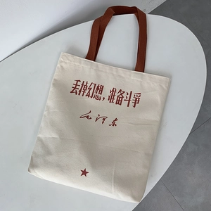 Detail of canvas tote bag with brown handles and red slogan print on a white surface