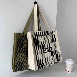 Minimalist geometric pattern canvas tote bags in army green and off-white hanging on a wall