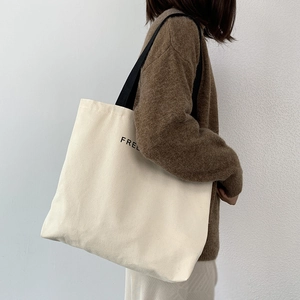 Detail of minimalist canvas tote with black strap and letter print on off-white fabric