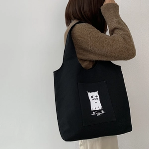 Detail shot of black canvas tote bag featuring cute white cat graphic and front pocket