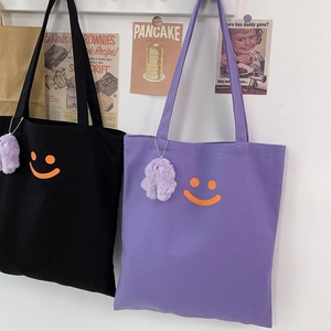 Detail of canvas tote bags with smiling face print and purple plush monster charms