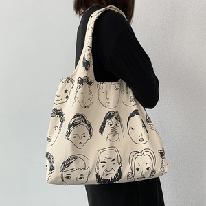 Detailed side view of beige canvas tote bag with artistic black and white face graffiti