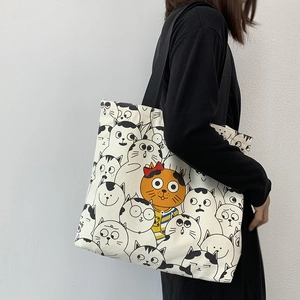 Detail of canvas tote bag featuring cute cartoon cat patterns and black shoulder strap